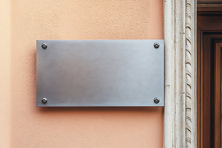 Close-up captures a sleek, horizontal silver sign mounted on a textured orange wall, secured by four screws. A decorative door frame adds an architectural element, view.の素材