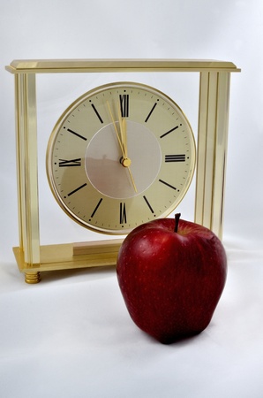 Red apple in foregound reflecting in brass clock in background set one minute to midnight on white felt.の写真素材