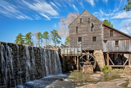 Old rustic mill in North Carolina with waterfall in foreground and tall pine trees, mill and mill wheel in background.の写真素材