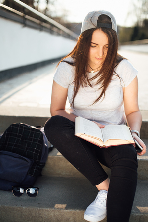 Pretty girl sit on the steps and read book with headphonesの写真素材