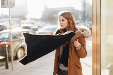 Young pretty girl walk on the street. Hang her scarf in one hand and look around. Winter clothing with warm weatherの写真素材