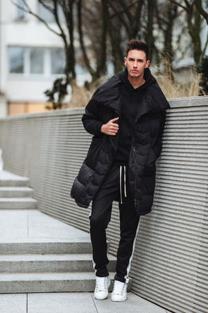 Fashionable man stand on the street near buildings. Winter, autumn outfit. Jacket with blouse and white sneakers. の写真素材