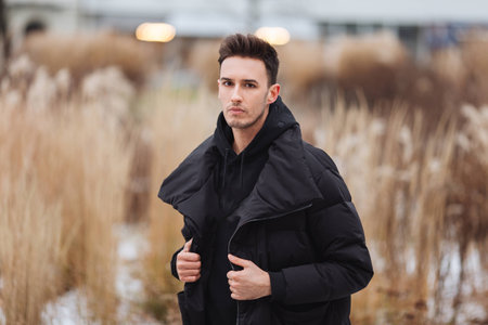 Stylish man wolk on the street. Winter cold outfit. Big jacket with white sneakers. Blured background street. Profecional model photo. の写真素材
