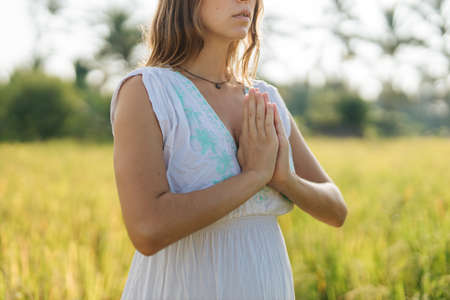 Pregnant woman stand at the field with green grass and fold her hands in pray. Sunshine summer vibes