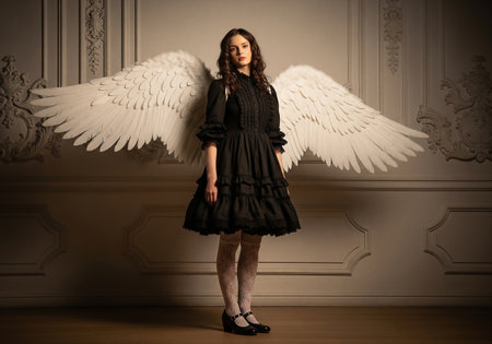 Beautiful young woman in black dress with angel wings in the interiorの素材