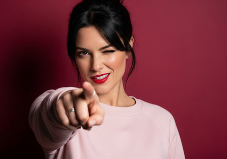 Portrait of a beautiful young woman pointing at the camera on a red backgroundの素材