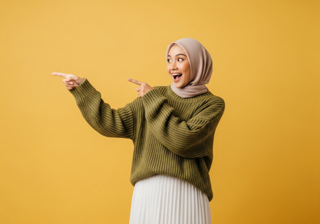Portrait of a happy muslim woman pointing at copy space isolated over yellow backgroundの素材