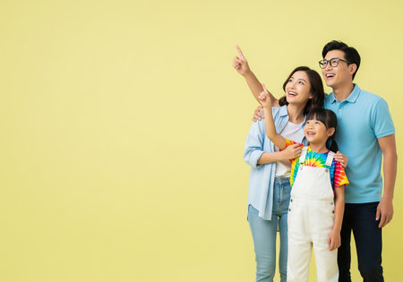 Happy asian family standing and pointing at copy space isolated on yellow backgroundの素材
