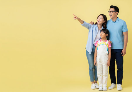 Happy asian family with daughter pointing at copy space on yellow backgroundの素材