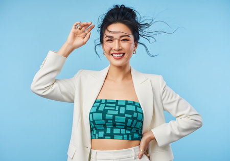 Portrait of a happy young asian woman in white jacket posing over blue backgroundの素材