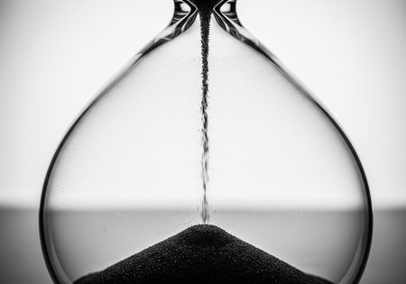 Close-up of an hourglass with flowing sand on a white backgroundの素材