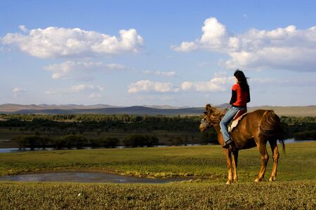 An asian girl horse riding at the grassland.の写真素材