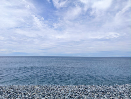 Seashore with pebbles and blue sky with white cloudsの写真素材