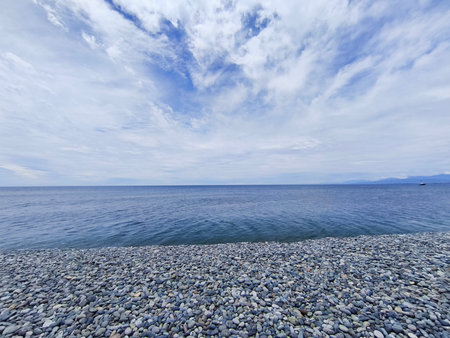 Blue sky with white clouds over a pebble beach in summerの写真素材