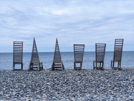 Row of wooden chairs on a pebble beach by the seaの写真素材