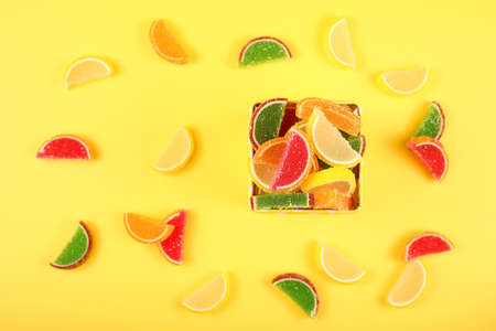 multi-colored marmalade in the form of orange slices in a square bowl on a yellow background