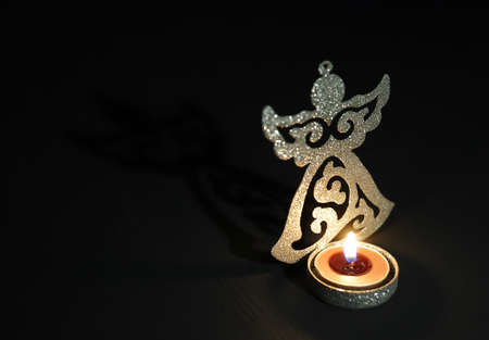 Silver candlestick in the shape of an angel with a burning candle in the dark