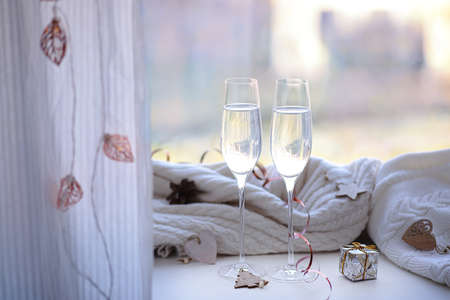 Two glasses of champagne and a gift on the windowsill decorated with Christmas tree wooden toys with a garland and pine conesの写真素材