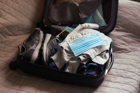 Open suitcase with clothes pills with anti-virus masks on fabric backgroundの写真素材