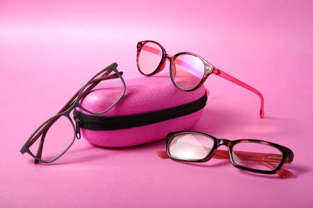 Three pairs of different glasses on a pink glass case on a pink background