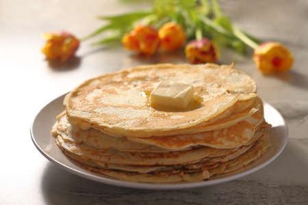 pancakes on a white plate with butter on a background of yellow flowersの写真素材