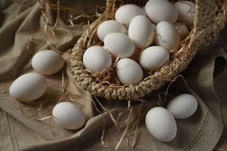 wicker basket with white eggs on a canvas, decorated with paper hay. easter concept.