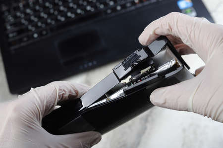 Computer battery in hands in gloves on the background of a laptop