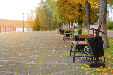 Vintage forged metallic bench on river embarkment with paving stones road with bright autumn leaves. autumn landscape.の写真素材