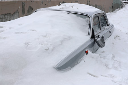 Gray car with a broken rearview mirror under a layer of snow. View from the front.の写真素材