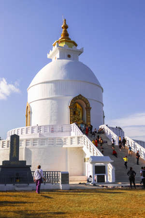 Close-up view of World Peace Pagoda showing tall Buddha statue and stupa. People visiting buddha stupa located in Pokhara, Nepal.のeditorial素材