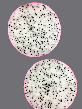 Close-up view of dragon fruit sliced in half showing small black seeds inside it on a plain backgrorundの写真素材