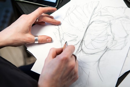 Girl tattoo artist draws a sketch with a sheet of Monstera. Close-up of hand drawing with a creative workplaceの写真素材