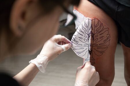 A professional tattooist is presented with sketch on the body of the girl in the Studio. Girl master and modelの写真素材