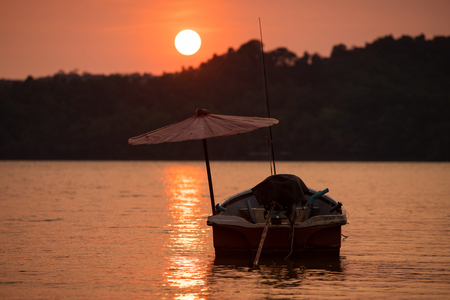 Fishing boat in contra light with umbrella at Golden sunset in calm evening seaの写真素材