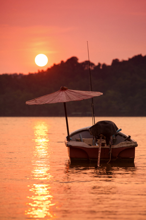 Fishing boat in contra light with umbrella at Golden sunset in calm evening seaの写真素材