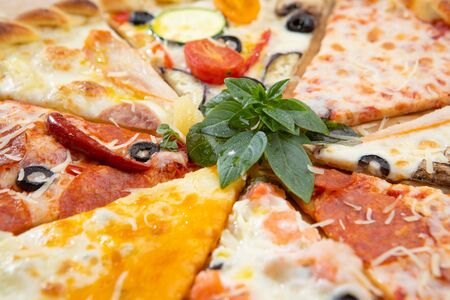 Assorted pizza slices close-up with different ingredients decorated with Basil, an assortment of traditional Italian fast foodの写真素材