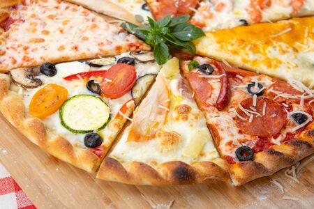 Assorted pizza slices close-up with different ingredients decorated with Basil, an assortment of traditional Italian fast foodの写真素材