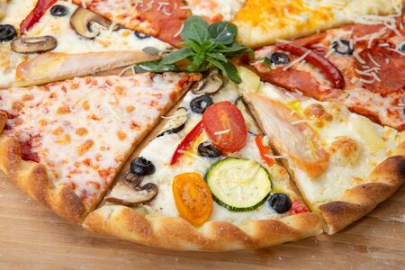 Assorted pizza slices close-up with different ingredients decorated with Basil, an assortment of traditional Italian fast foodの写真素材