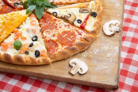Pizza assorted pieces on a Board on a checkered tablecloth decorated with mushrooms and Basilの写真素材
