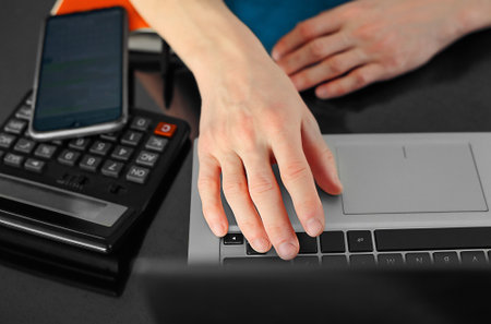 Close-up of men's hands typing on a laptop keyboard, a mobile phone and a calculator on a tableの写真素材