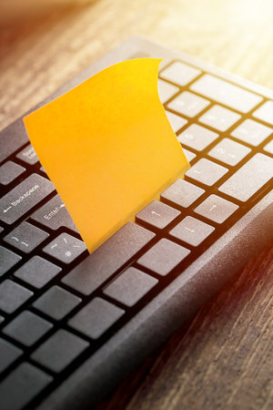 Computer keyboard and sticky note on wooden background.の写真素材