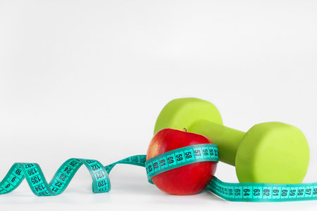 fresh delicious red apple and green dumbbells, with measuring tape, on a white background, close-up. Healthy lifestyle, fitness sportsの写真素材