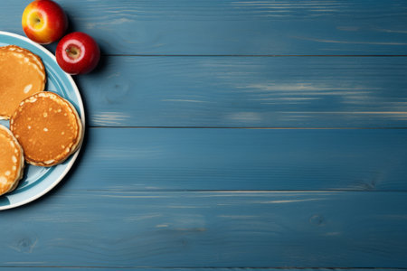 The pancakes are on a light blue plate with two apples on a blue wooden background. a place for a text or recipe.の素材