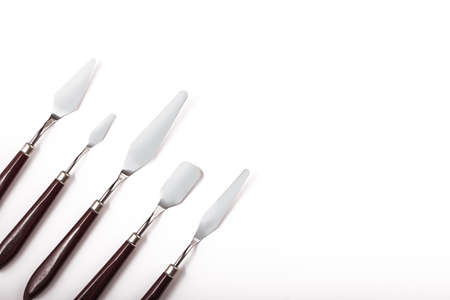 Five art palette knives lie on a white background.Stainless steel painting palette knife isolated on...