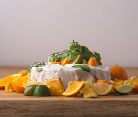 Fruit cake with cream, lime and oranges on table with light backgroundの写真素材