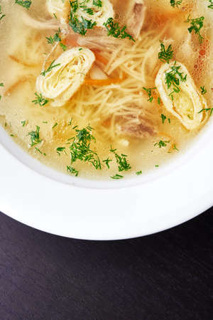 Clear chicken broth with vegetables and noodles on black backgroundの写真素材