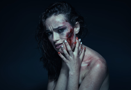 Beautiful girl with a scar on her face in the blood on a dark backgroundの写真素材