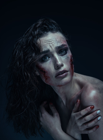 Beautiful girl with a scar on her face in the blood on a dark backgroundの写真素材