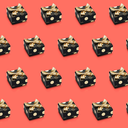 Diagonal sparse lines of black wrapped present boxes on red. Living coral color background. Gift design with gold tape, bows, circles, dots pattern. Top view. Geometric, abstract texture.の写真素材