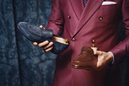 Close-up of businessman standing in modern showroom and holding fashionable footwear. Smart fashion designer presenting best type of stylish shoes. Bootmaker workshop conceptの写真素材